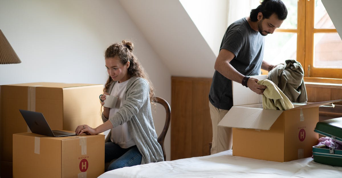 Where in Seoul can I rent a laptop? - Pensive female surfing internet on netbook and drinking coffee while ethnic man unpacking belongings from cardboard box after moving into new attic style house