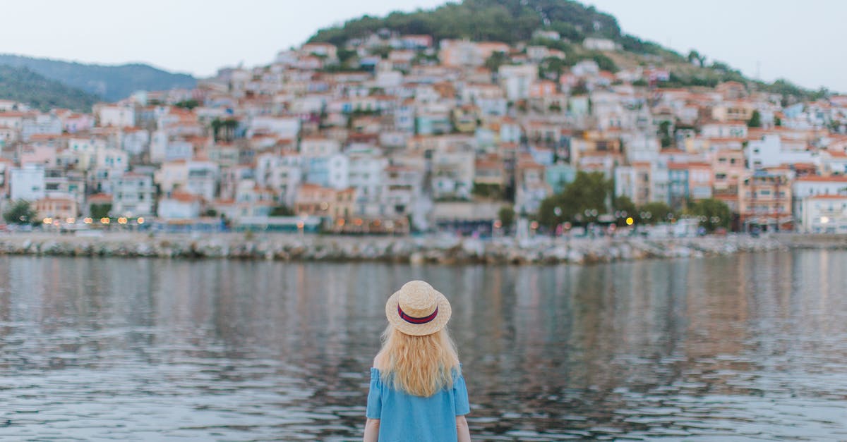 Where in the world is this harbour town? - Back View of Woman in Blue Dress Sitting on the Shore