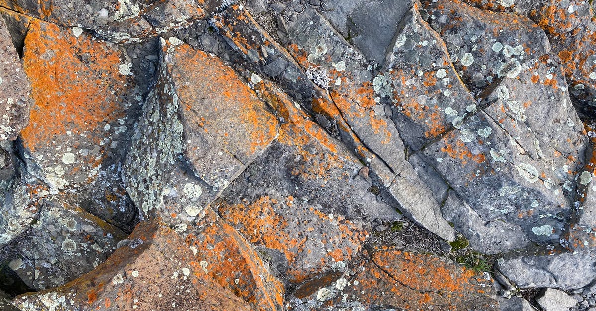 Where is the cheapest place on earth to rock climb? - Top view of rough natural rock surface with cracks and orange rust as abstract  background