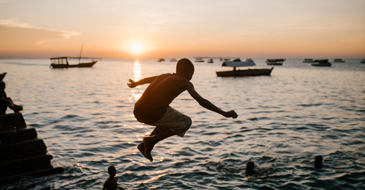 Where is the highest Bungee jump above sea? - Back view of anonymous ethnic teen boy in moment of jumping in sea water at sunset