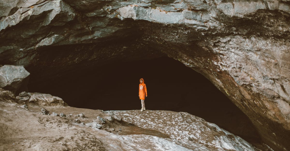 Where is there this large rock in the French Riviera? - Full body of faceless person in warm clothes standing alone in dark cave of large stone mountain