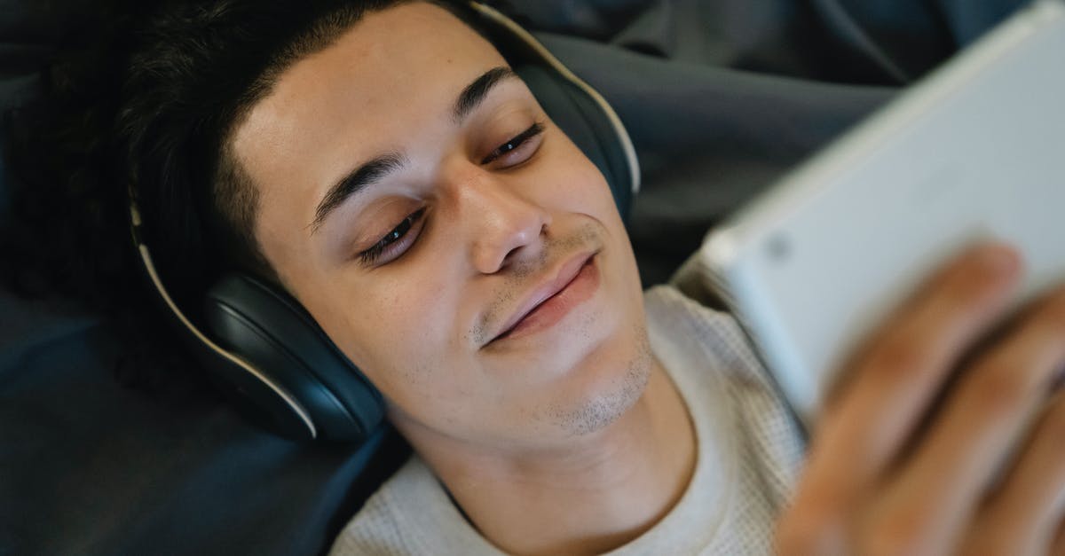 Where is this location from the "A 1000 Times" music video? - Positive young Hispanic man in headphones smiling and watching film on tablet while relaxing on bed at home