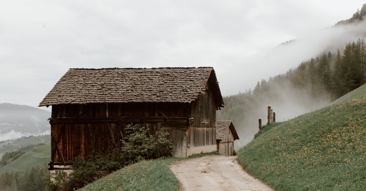 Where is this ridge in Charlevoix, Québec? - Old rural brown houses with triangle roof on mountain slope covered with grass and yellow flowers next to road and forest on mountain in fog