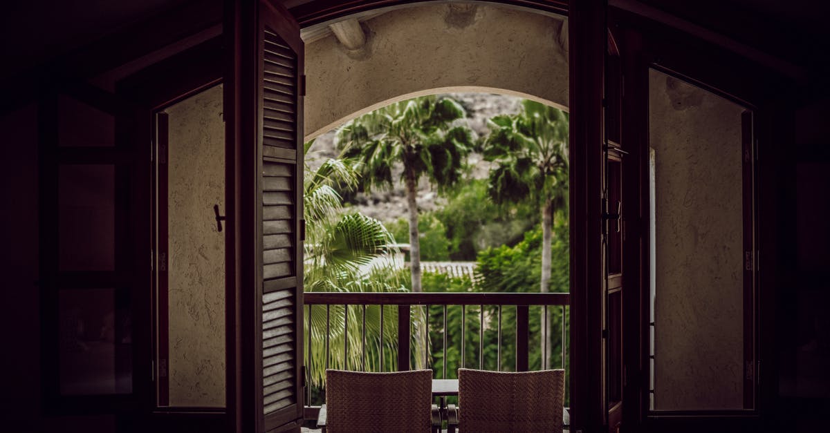 Where is this steeple, these palm trees, flats in Hong Kong? - Interior of empty dark room with chairs near doorway on balcony with railing next to palms in daylight