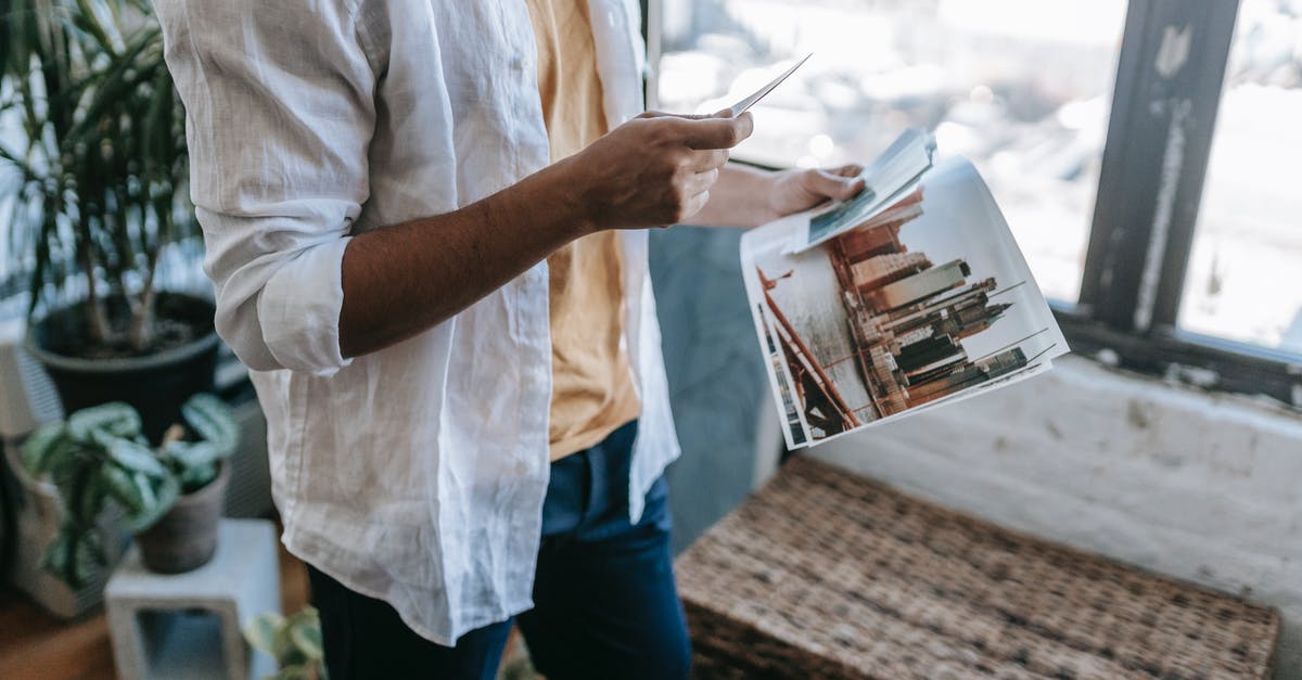 Where on earth is this image from the backgrounds in Windows? - Crop anonymous male wearing casual clothes looking at printed pictures in hands while standing near window in modern living room