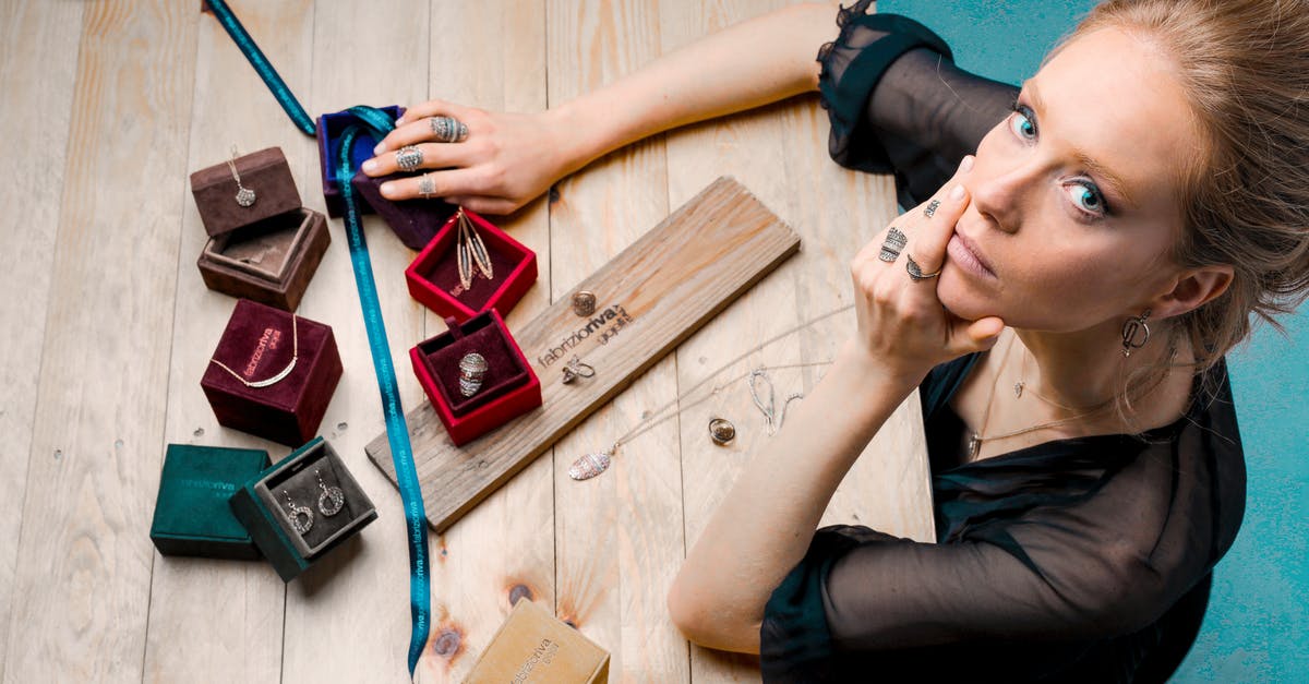 Where to find music workshops in Hanoi? - From above serious businesswoman looking up at camera while sitting at wooden table with small jewelry boxes with bijouterie and decorating with ribbon as present