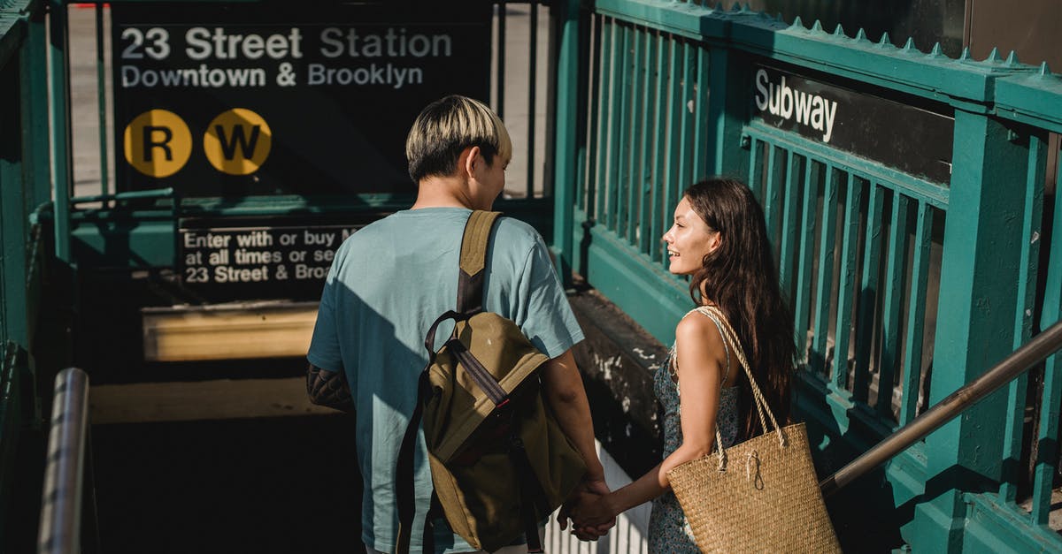 Where to meet a travel partner at the Hong Kong airport? - Back view of young happy diverse couple with bags looking at each other near underground Where to meet a travel partner at the Hong Kong airport? - Back view of young happy diverse couple with bags looking at each other near underground