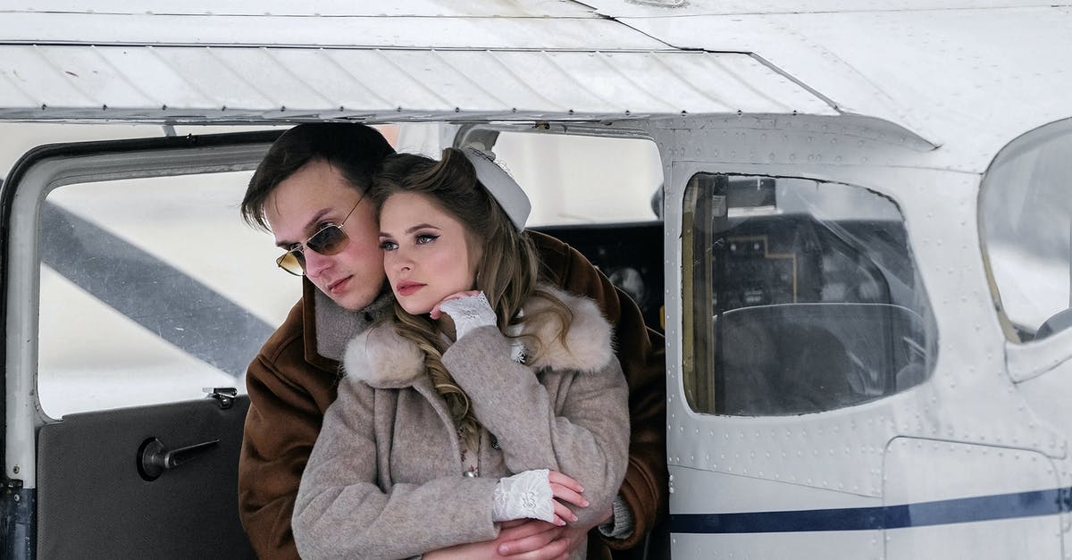 Where to meet a travel partner at the Hong Kong airport? - Stylish young couple in warm coats hugging gently near modern private jet and looking away on cold winter day Where to meet a travel partner at the Hong Kong airport? - Stylish young couple in warm coats hugging gently near modern private jet and looking away on cold winter day