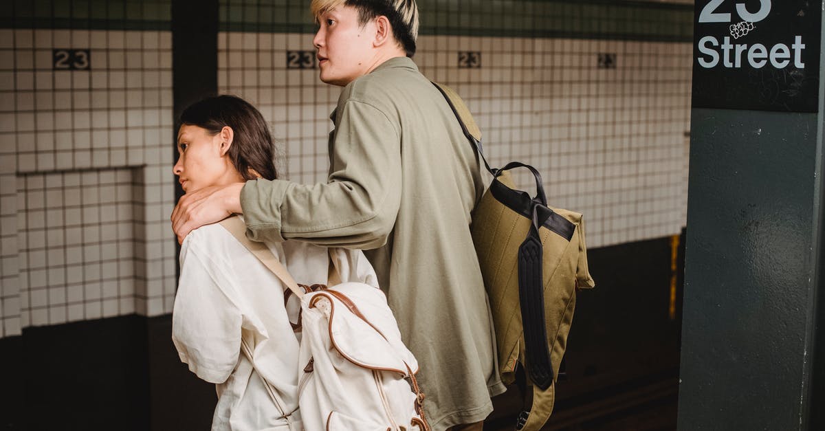 Where to meet travel partner at JFK (Terminal 4 arrivals) - Back view of Asian couple with backpacks hugging and standing on platform of subway station and leaning forward while waiting for train