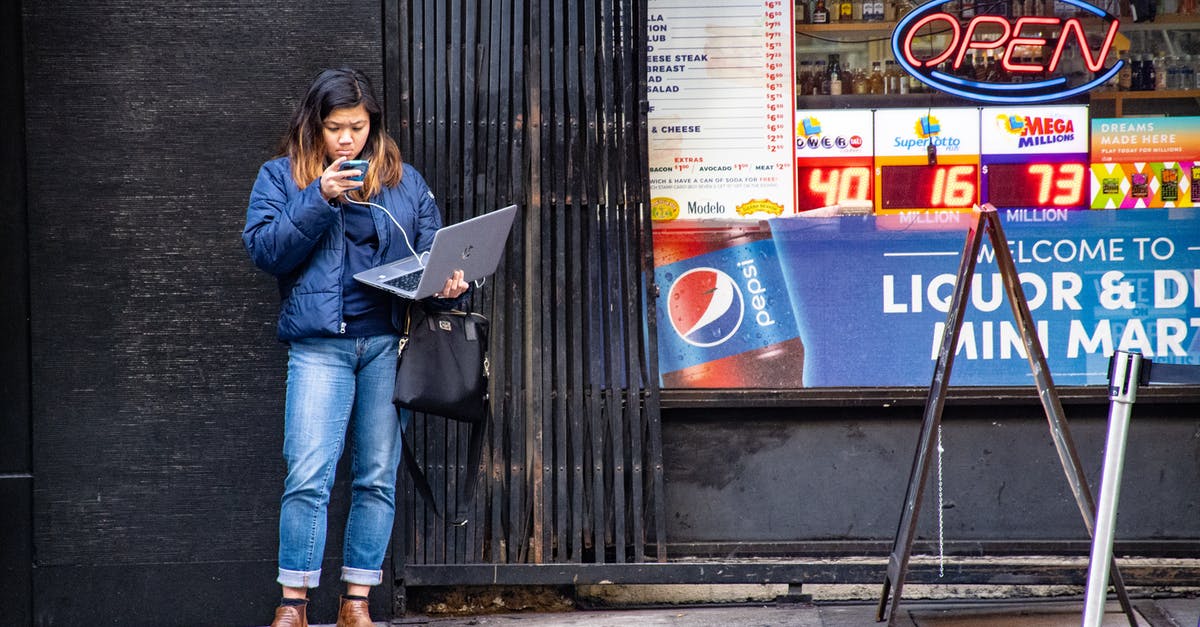 Where to store a laptop while doing few days trips during a long-term travel? - Woman in Blue Jeans Holding Macbook Pro Standing Against Black Wall Where to store a laptop while doing few days trips during a long-term travel? - Woman in Blue Jeans Holding Macbook Pro Standing Against Black Wall