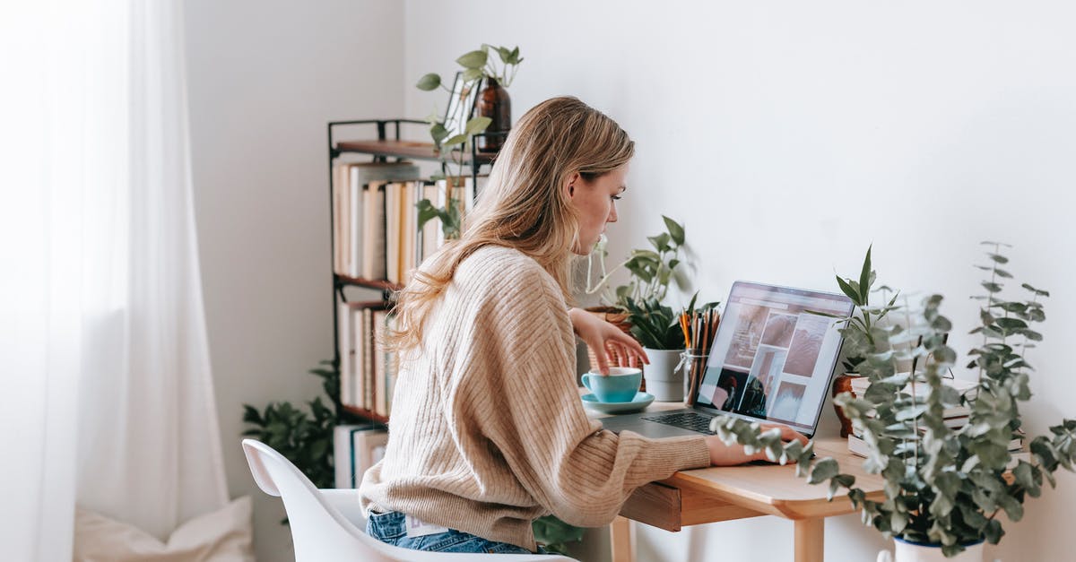 Where was this photo taken? - Side view of attentive female remote employee with cup of tea watching photo gallery on netbook screen at desk in house