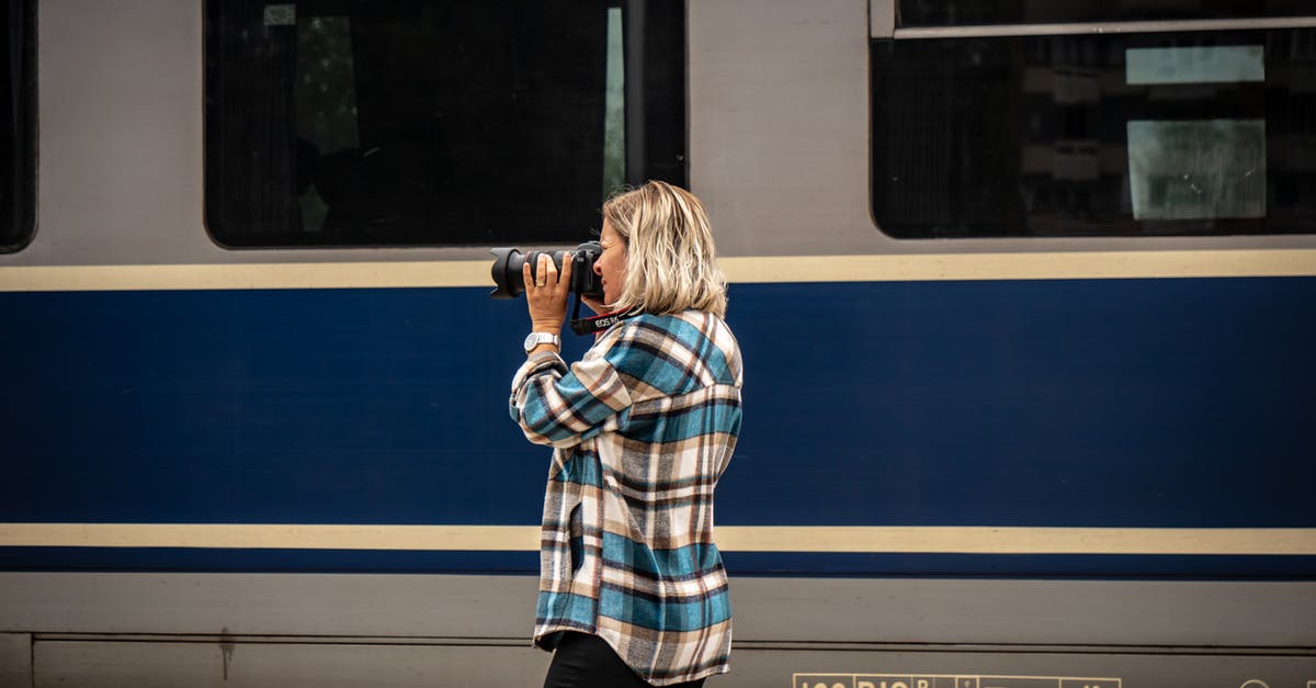 Where was this train photograph taken? - Woman in Blue White and Black Plaid Dress Shirt and Black Pants Standing Near Blue and