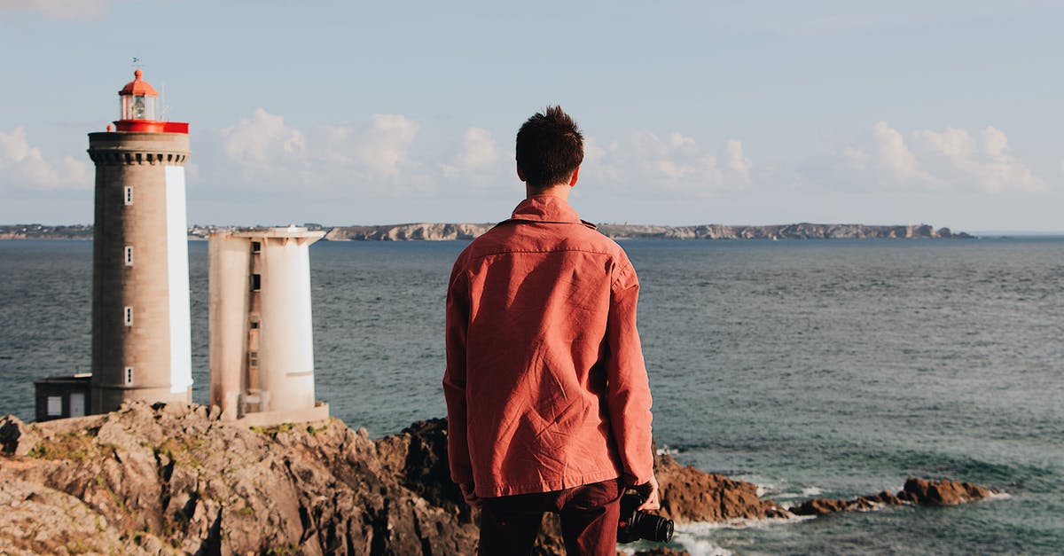 Which AA Admirals' Club location at DFW is most comfortable? - Back view of unrecognizable male traveler in casual red clothes contemplating seascape while standing on rocky shore with lighthouse near rippling sea