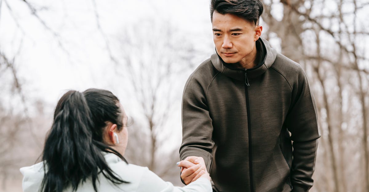 Which consulate will give me the longest Schengen visa? - Calm Asian man in sportswear giving hand to unrecognizable female with dark hair in earphones in autumn park in daytime