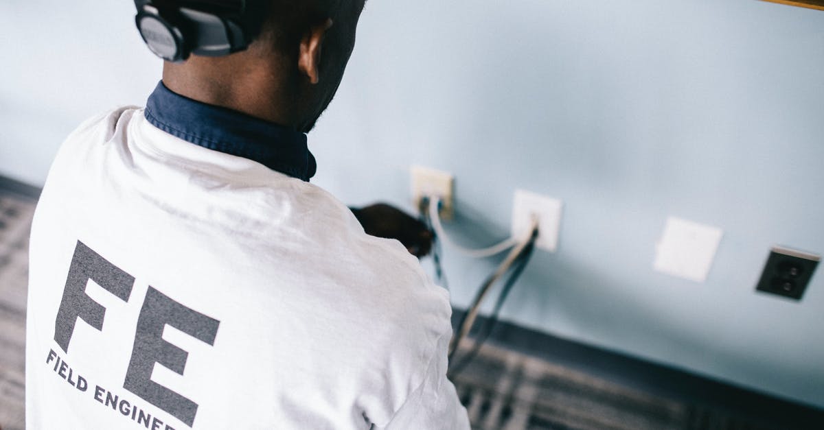 Which electrical plugs are used in Thailand? - From above back view unrecognizable black field engineer wearing white shirt and protective hardhat sitting on floor and checking voltage in wall plugs