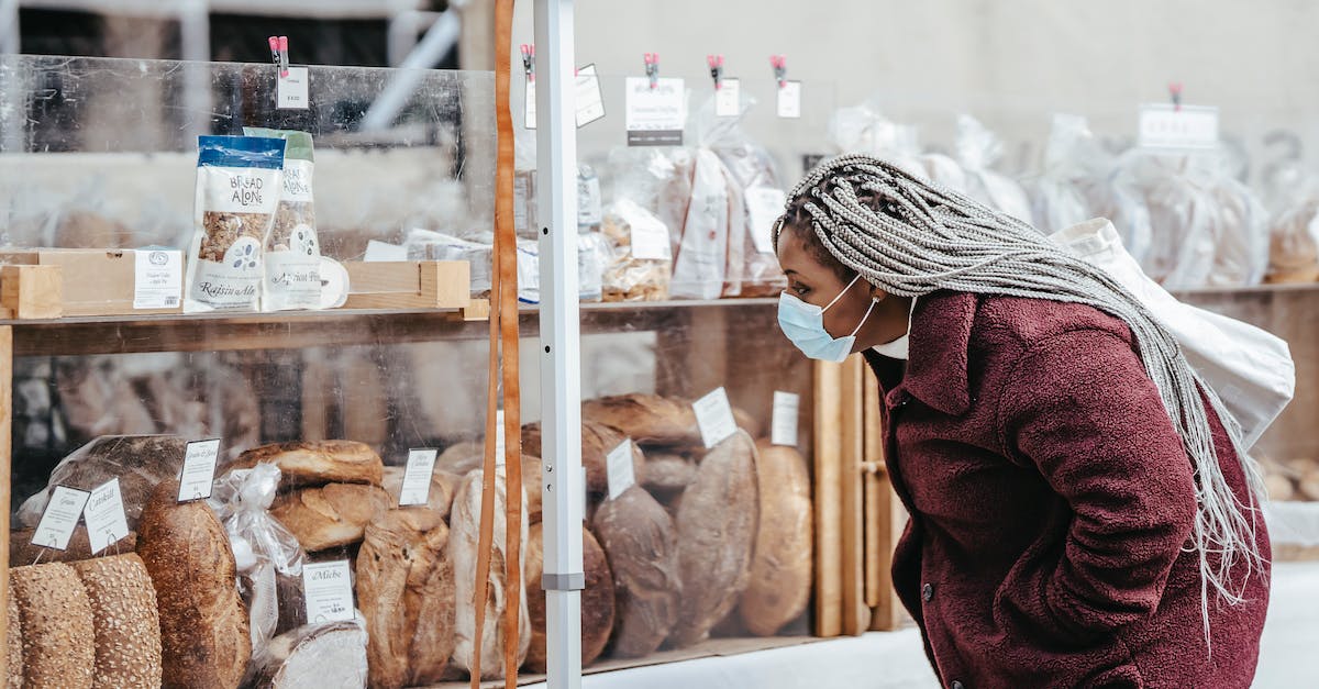 Which website to use when choosing local US flights? - Side view of adult black lady wearing protective mask and warm coat selecting baking goods while standing in street market in daytime