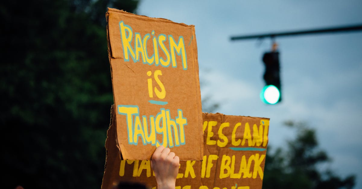 Who is responsible for the refund policy on a code-share flight? - Crop anonymous activist demonstrating placard with racism is taught text while protesting for Black Lives Matter movement in evening