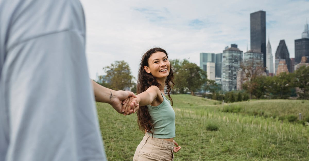 Why did TSA pat me down at Rochester NY airport? - Crop anonymous man holding hand and following happy young ethnic girlfriend while spending time together in green park in New York