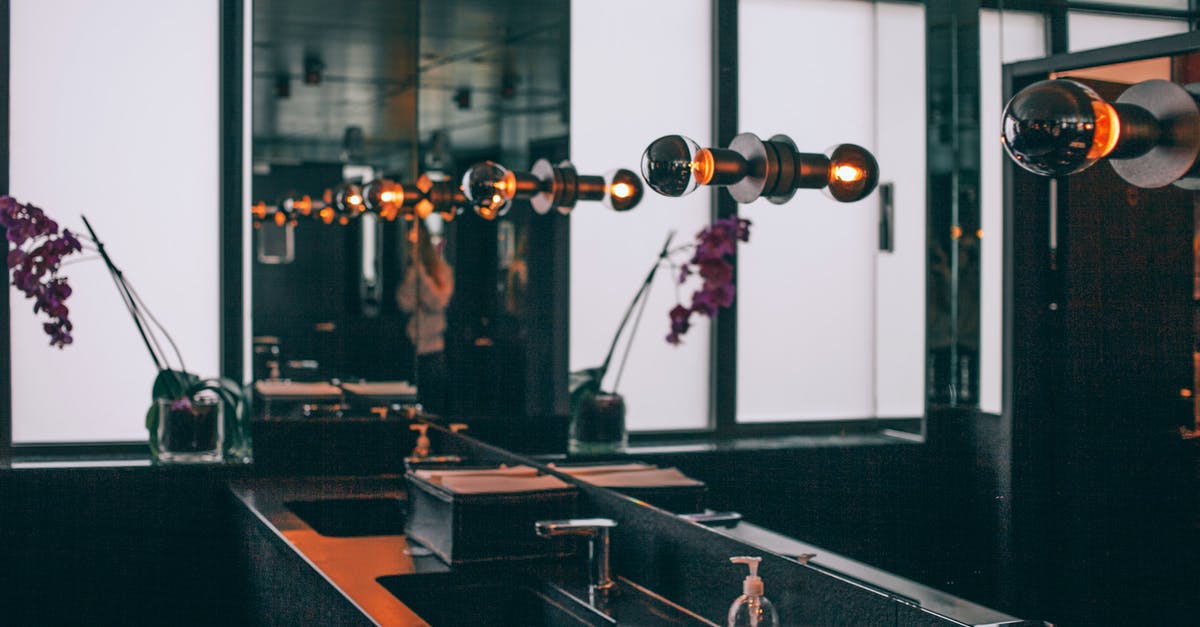 Why do many public bathrooms in Israel lack toilet seats? - Black sinks with stainless steel faucets placed under wide mirror decorated with illuminated dark lamps in modern toilet room