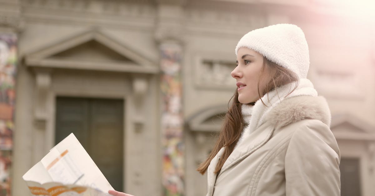 Why do people sit outside Primark Oxford Street West? [closed] - Side view of female traveler in warm clothes and head wear studying map while standing near antique building