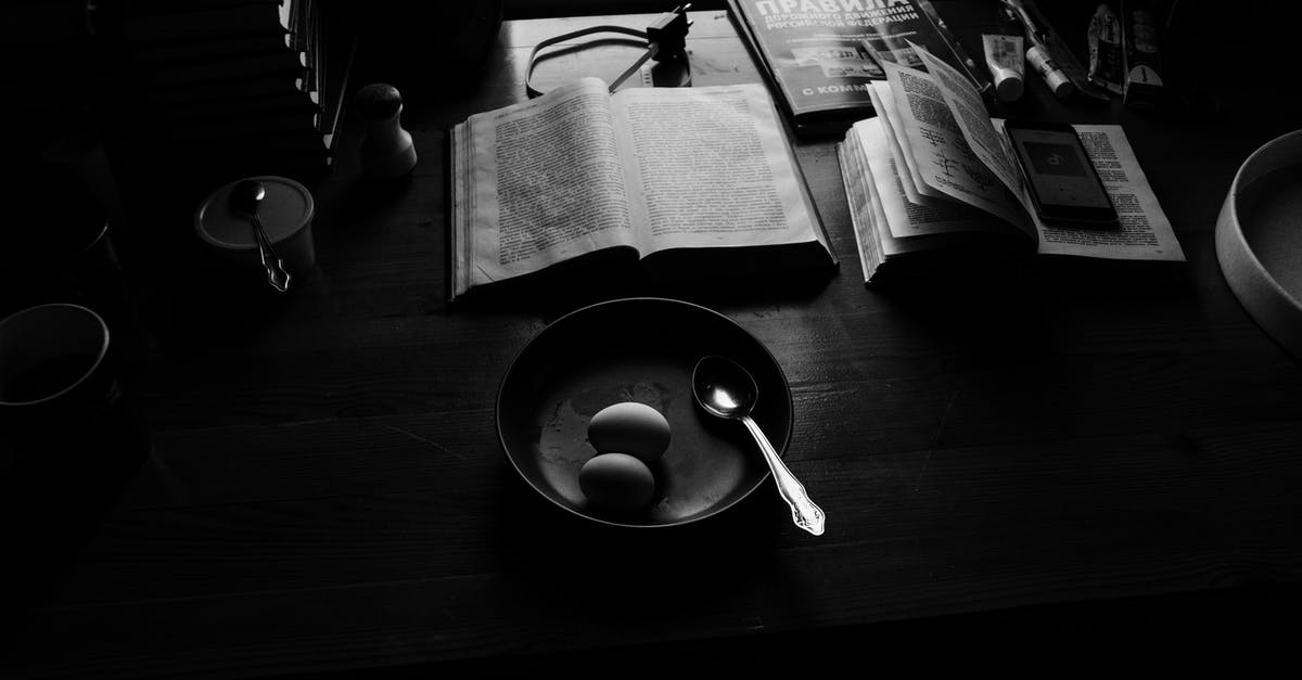 Why do some airlines charge more for break journeys - Black and white of plate with eggs and spoon near opened books and textbook and phone charger placed on wooden desk under light from window