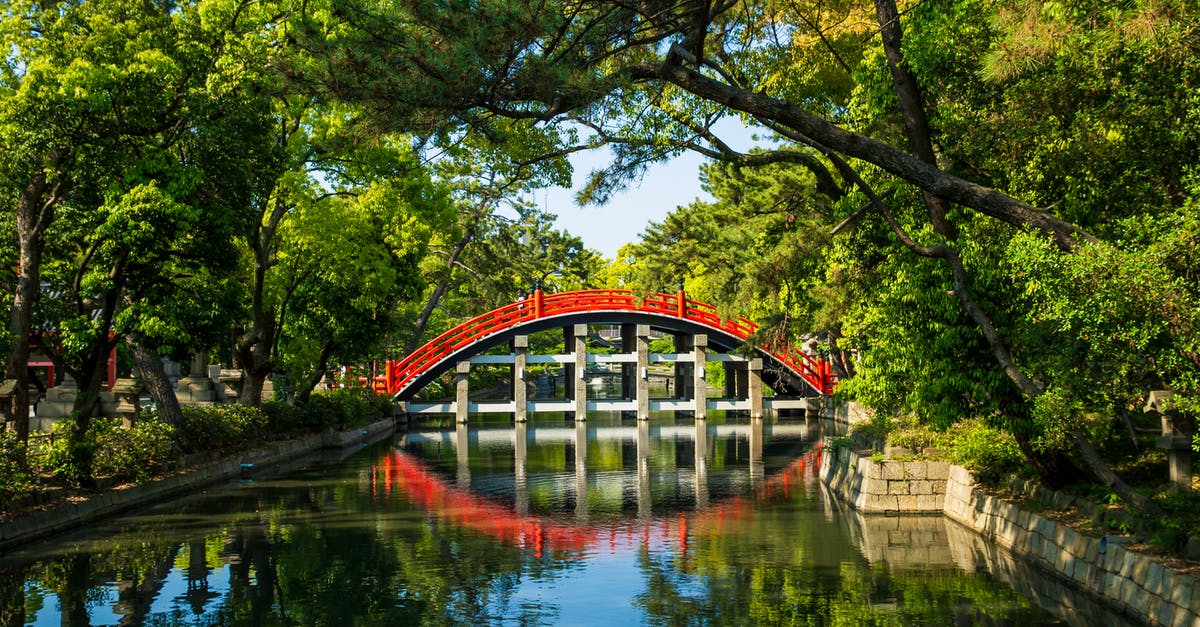 Why do taxis in Japan have mirrors on the hood? - Aged red bridge above water channel near trees in park