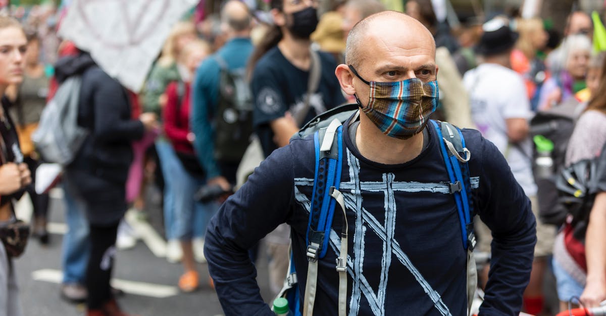 Why do UK people stand on the right on escalators? - Concentrated adult male in mask and with backpack standing in street near crowd of protesters