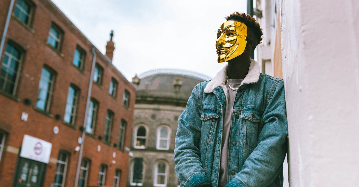 Why does Rotterdam not want me to lean against buildings? - From below of confident black activist in stylish outfit and famous Anonymous mask leaning on building placed in city district in daytime