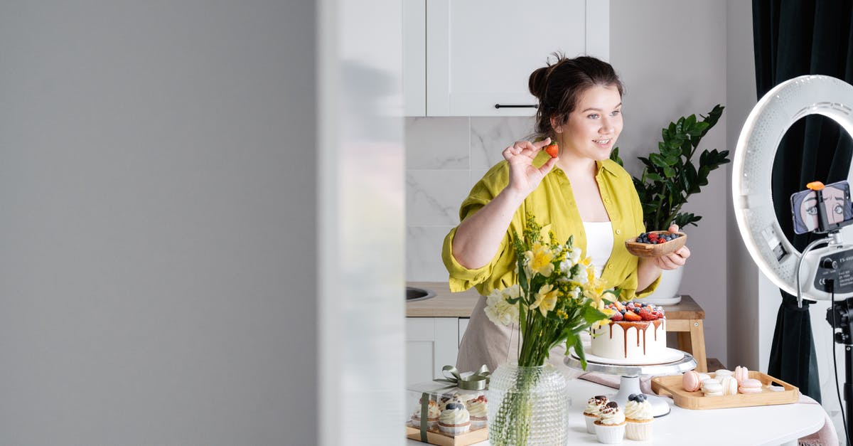 Why does the Eurostar not show youth pricing? - Delighted young female influencer in casual clothes smiling and demonstrating fresh berries while decorating appetizing cake during recording vlog on smartphone in kitchen