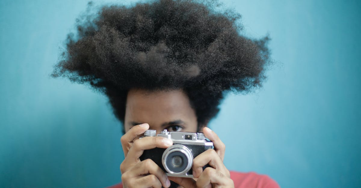 Why doesn't Saudi Arabia issue tourist visas? - Ethnic male with creative Afro hairstyle wearing pink t shirt taking pictures on retro photo camera against blue background while looking at camera