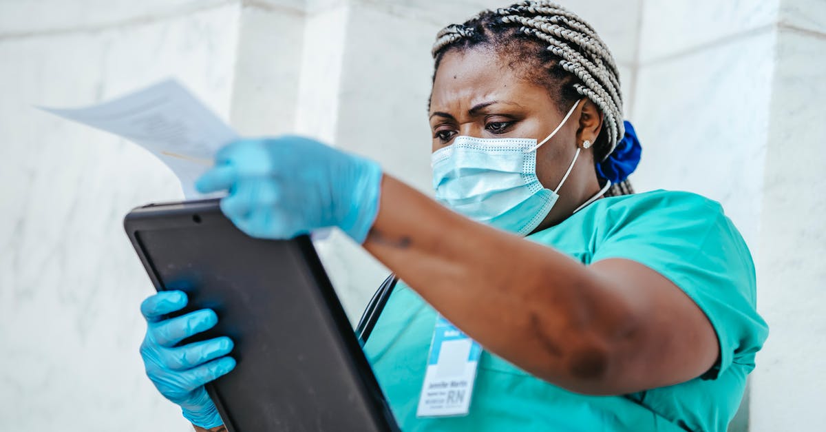 Why is a landing card required at UK border control? - Low angle of focused black female nurse in mask and gloves standing in hospital and looking through papers