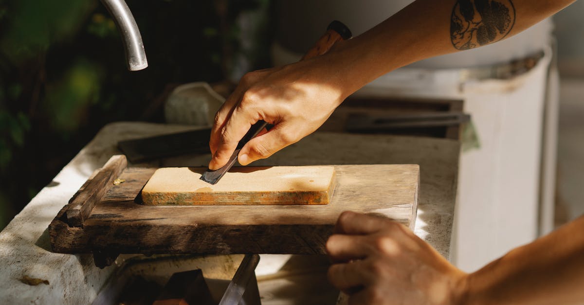 Why is the departures level always above the arrivals level? - High angle of crop anonymous tattooed woodworker flattening wooden block with sharp tool on old washbasin in sunlight