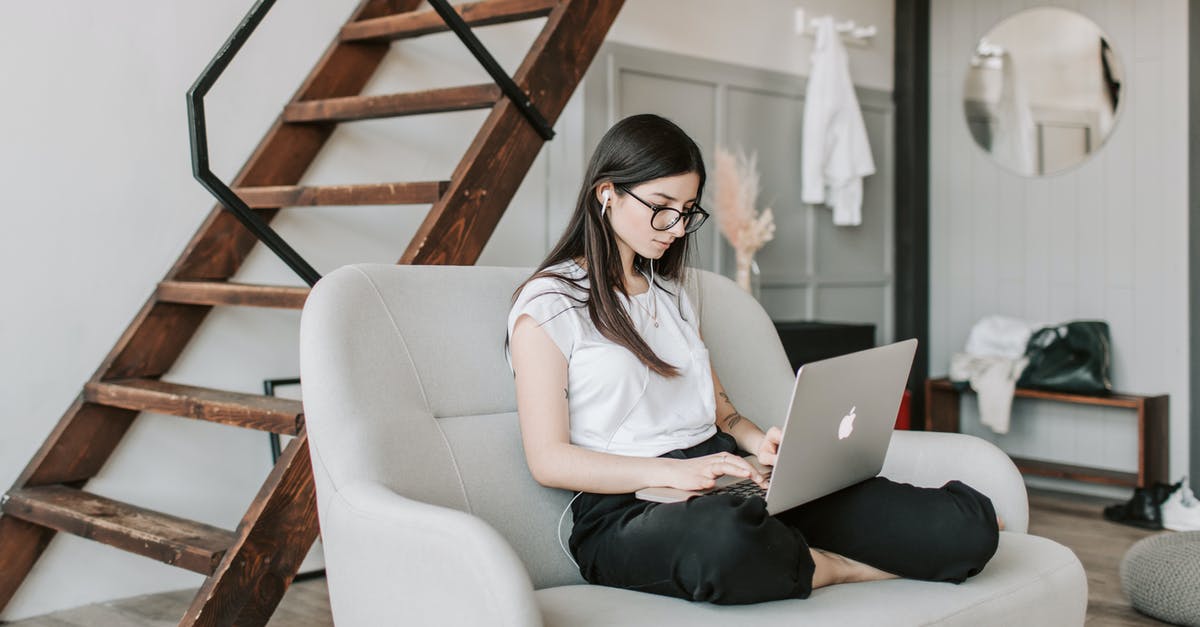 Why only earbud style earphones? - Young female in eyeglasses and casual clothes sitting barefoot on sofa in modern apartment with wooden staircase while wearing earbuds and watching movie on netbook