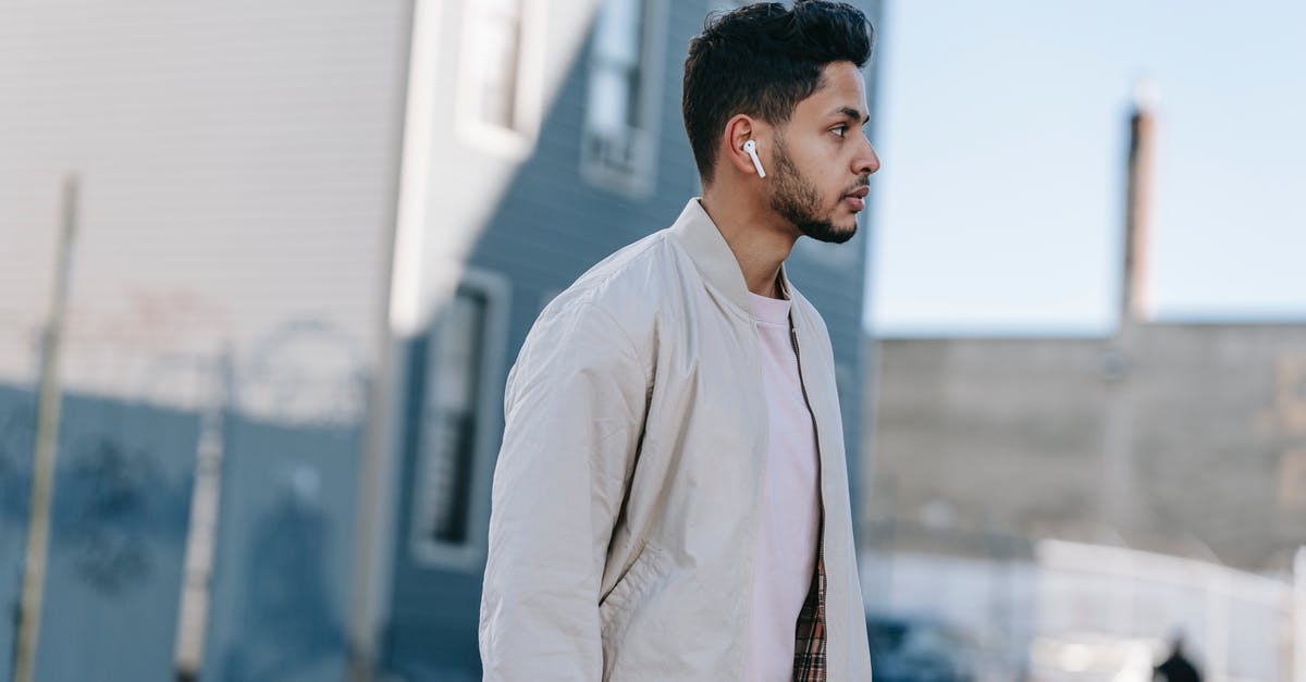 Why only earbud style earphones? - Side view of trendy ethnic male with modern haircut listening to song from earbud while looking away in city