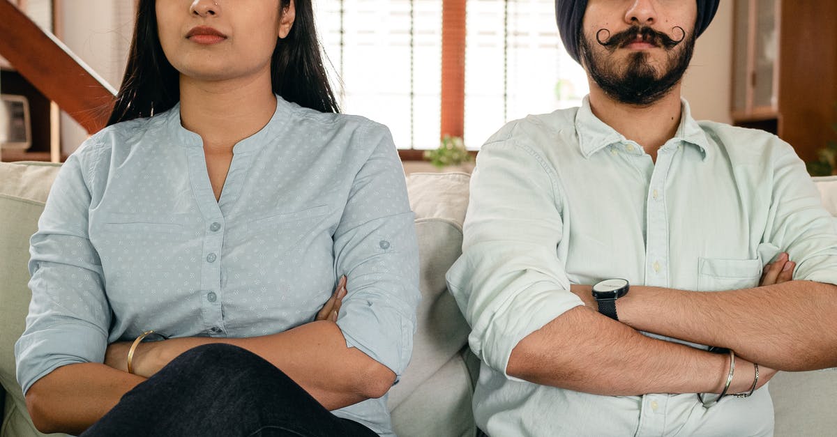 Wife applying for UK visa after husband got the decision? - Crop thoughtful young man and woman in casual clothes sitting on sofa with crossed arms after having argue