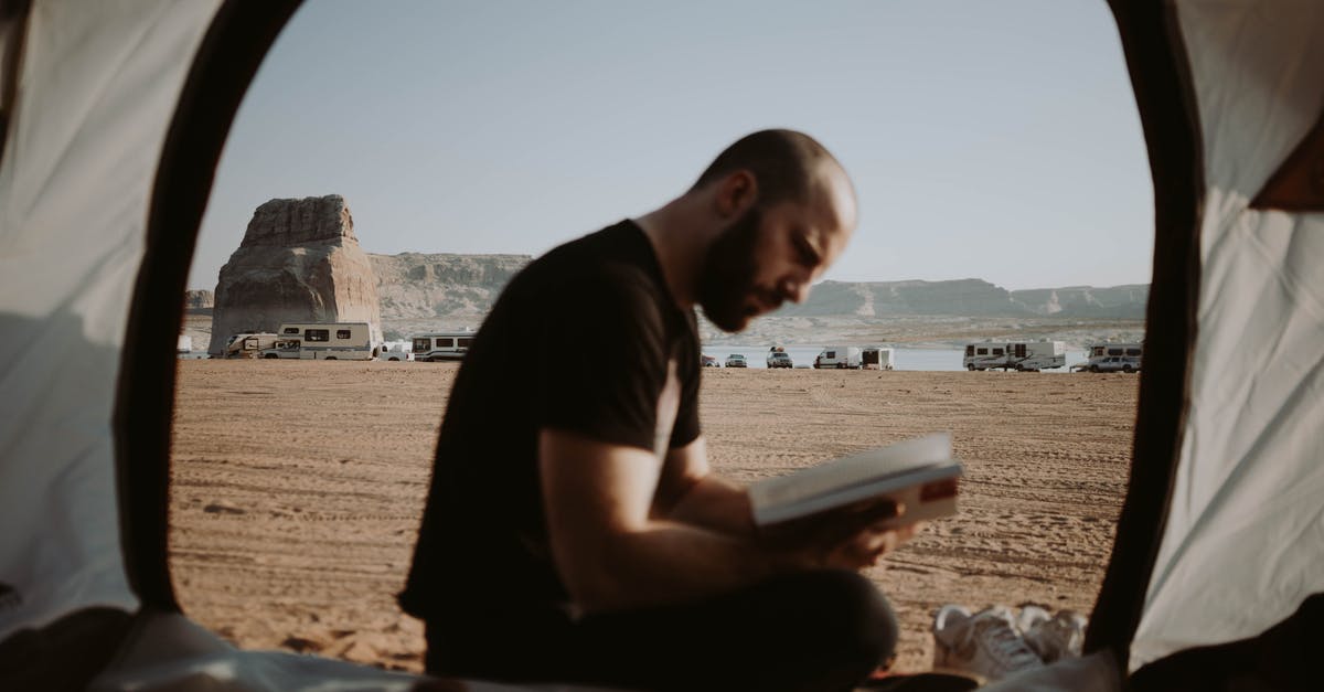 Wild Camping in Poland [closed] - Side view of bearded male traveler sitting in tent with opened door and reading book in nature with parked cars in distance