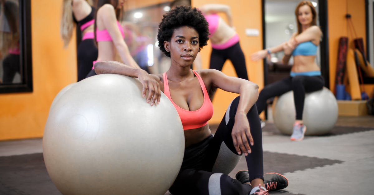 Will I fit in a first class airplane seat? - Young ethnic woman with fit ball sitting on floor while training in modern gym