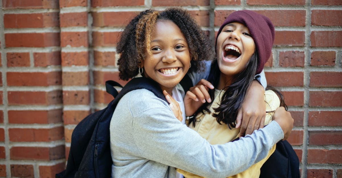 Will I have to recheck my bags? - Cheerful diverse schoolgirls embracing near brick wall