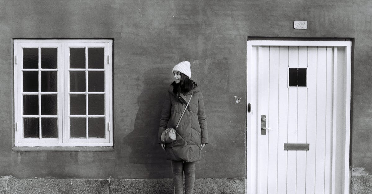 Will one be refused entry on a full passport? - Black and white full body of young female in warm outerwear standing near wall of residential house