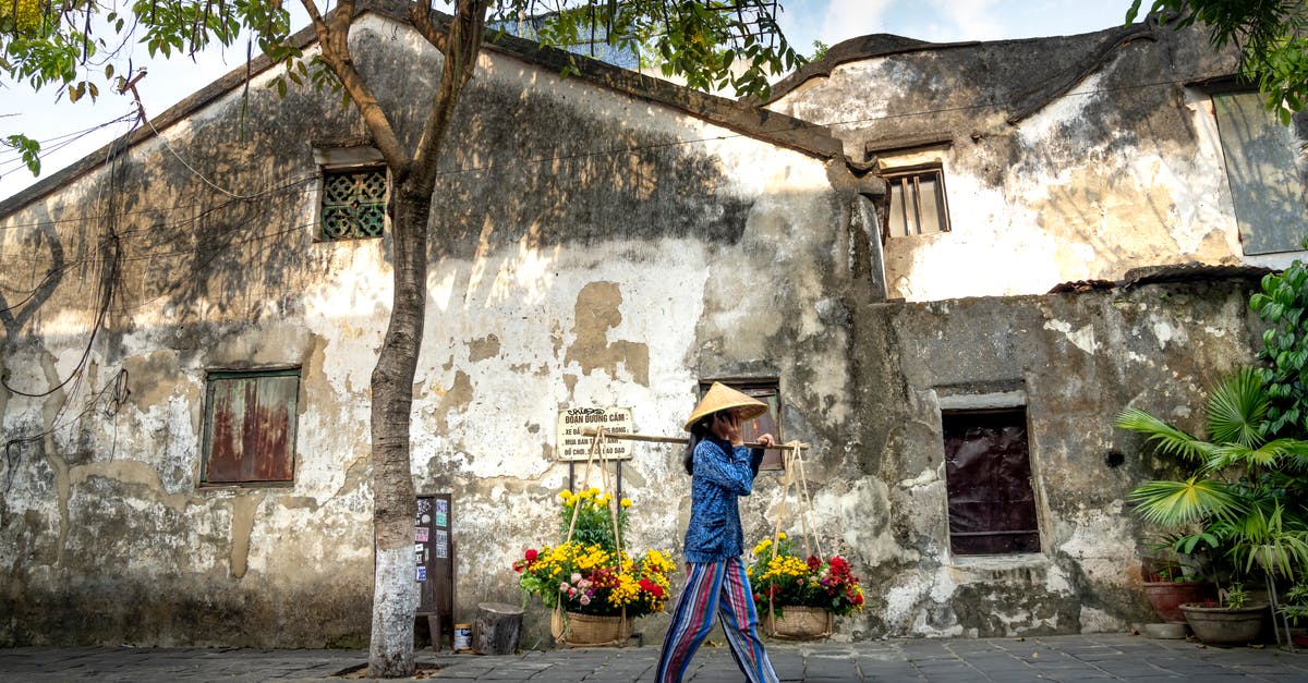 Withhold number when calling local numbers in Vietnam - Asian woman walking near shabby buildings and carrying baskets with flowers on street