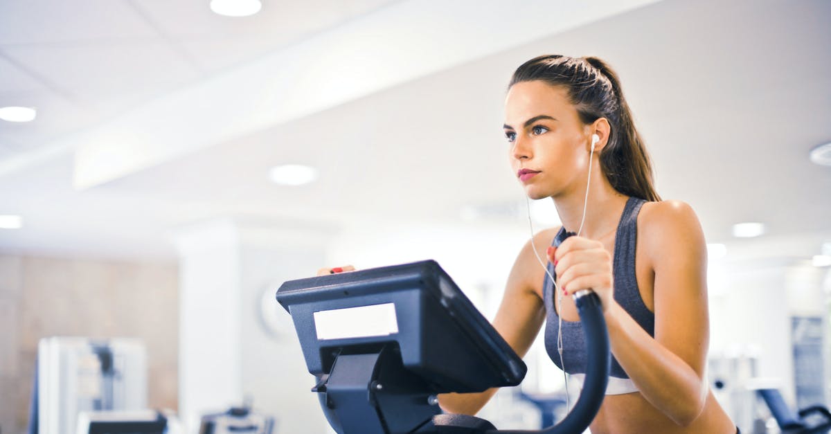 Wizz-air Discount Club companion travelling alone without the holder - Serious fit woman in earphones and activewear listening to music and running on treadmill in light contemporary sports center