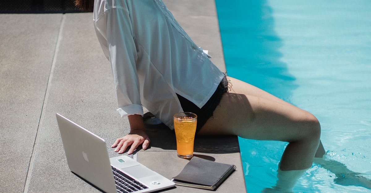 Working remotely on the French work and holiday visa? - From above side view of crop unrecognizable female traveler sitting on pool border with legs in water while relaxing after remote job on laptop