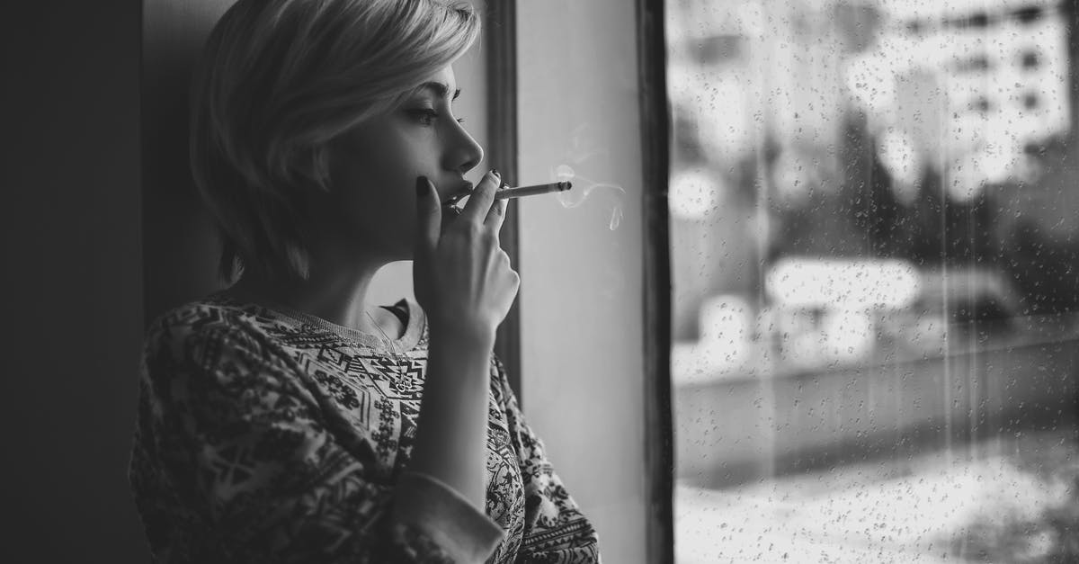 Worried about short layovers - Black and white depressed female with short haircut smoking cigarette and looking out window at rainy city