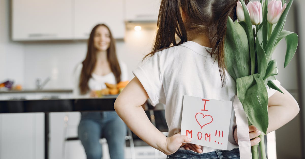 Would I be able to communicate in Vienna in German? - Back view of little girl with ponytails in casual clothes standing against mother with hands behind back and holding bouquet of tulips and drawing I love mom on kitchen