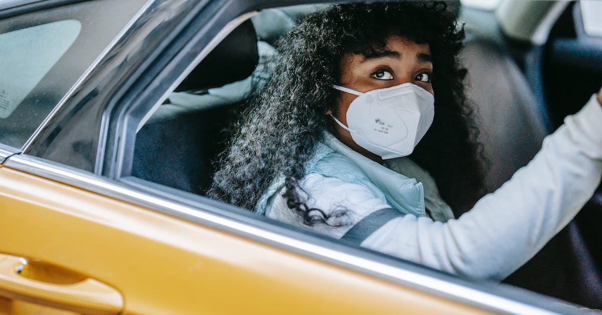 Would renting a car in Basel, Switzerland be safe for a foreigner? - Thoughtful African American female with dark curly hair in medical protective mask sitting in taxi and looking away in daytime